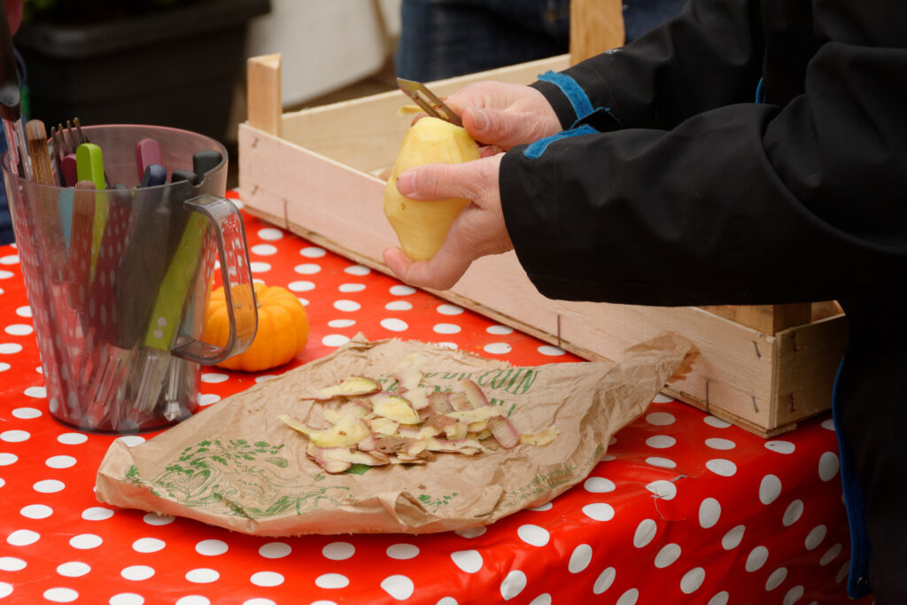 Photo d'une table de préparation champêtre avec une personne qui épluche une pomme de terre